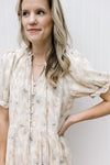 Close up of v-neck with a tie and covered buttons on a cream dress with floral and short sleeves.