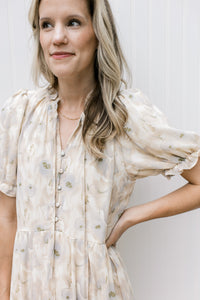 Close up of v-neck with a tie and covered buttons on a cream dress with floral and short sleeves.