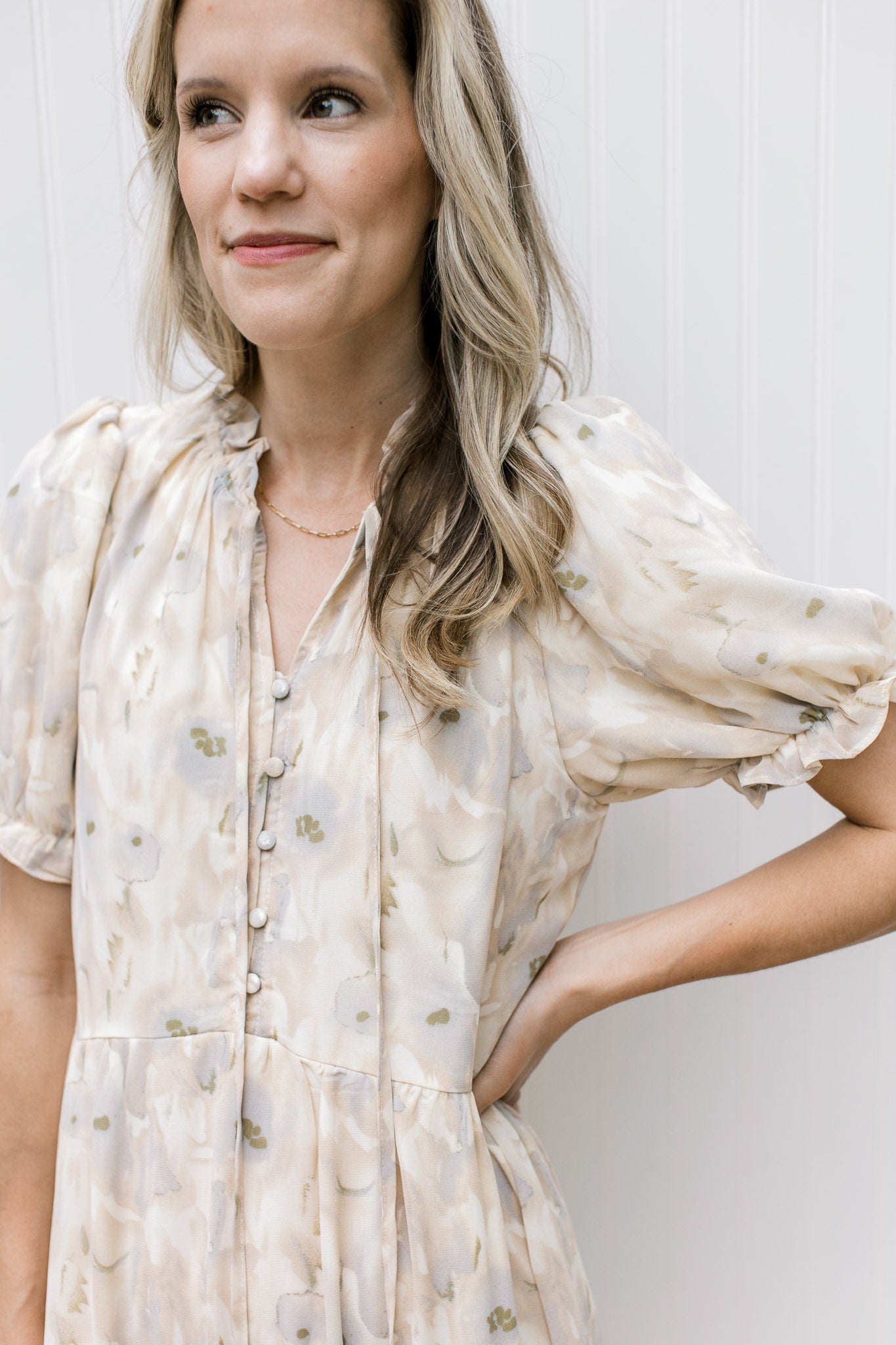 Close up of v-neck with a tie and covered buttons on a cream dress with floral and short sleeves.
