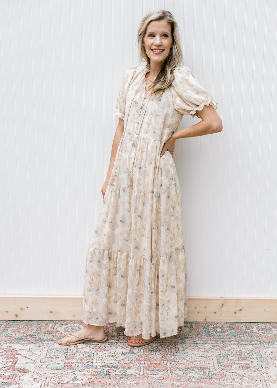 Model wearing sandals with a cream dress with watercolor flowers, short sleeves  and a tie v-neck.