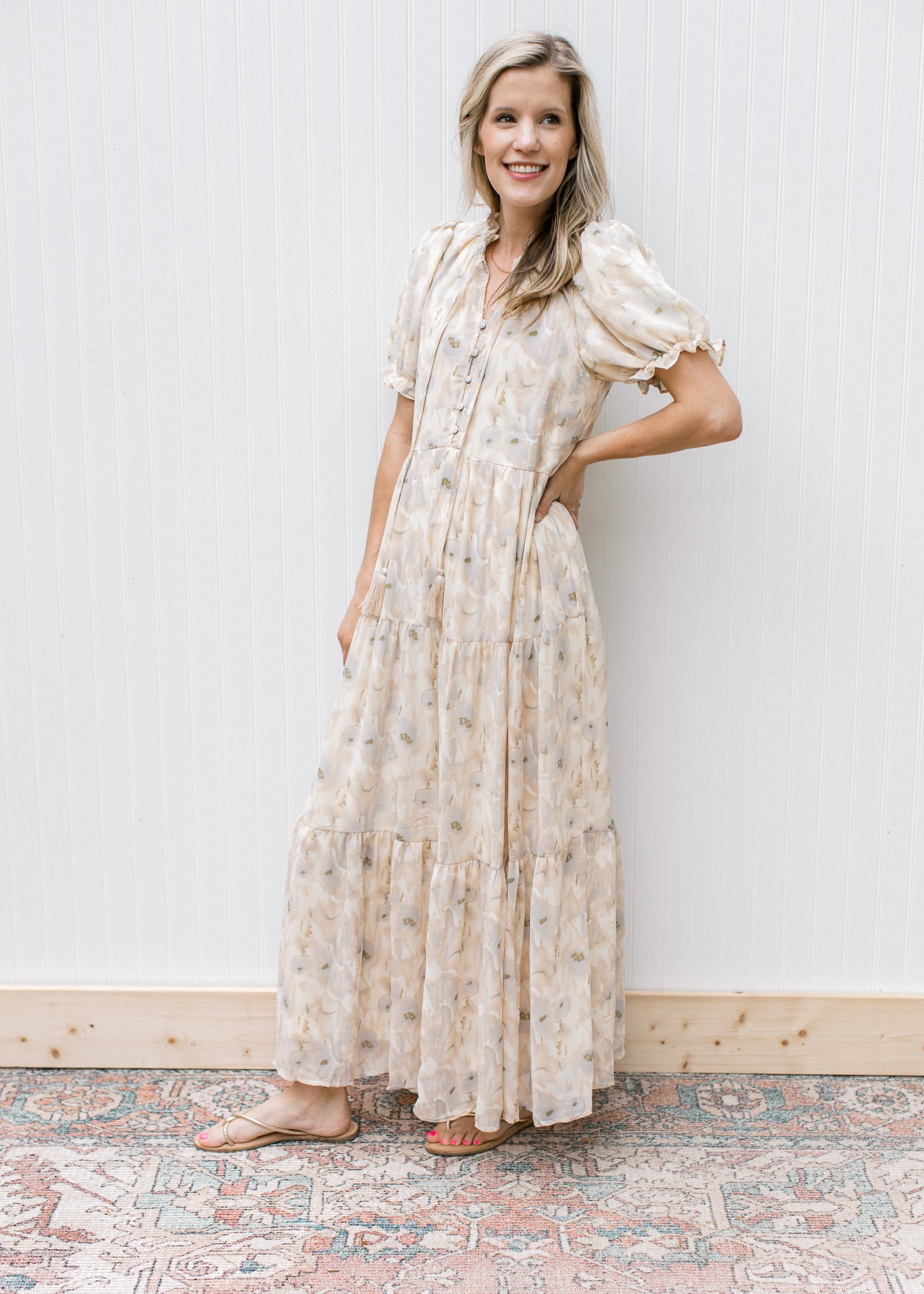 Model wearing sandals with a cream dress with watercolor flowers, short sleeves  and a tie v-neck.