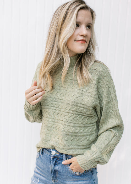 Model wearing a soft sage cable knit sweater with a mock turtle neck and long sleeves. 