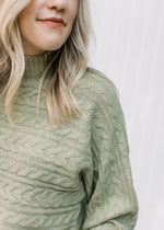 Close up of mock turtle neck and cable knit design on a long sleeve soft sage colored sweater. 