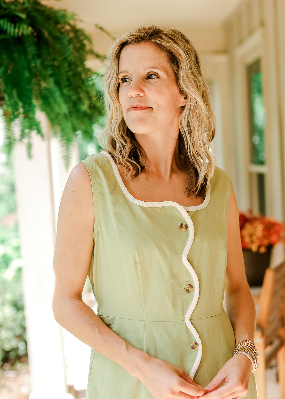 Model wearing a sleeveless light green midi with cream wavy piping, scoop neck and button front.