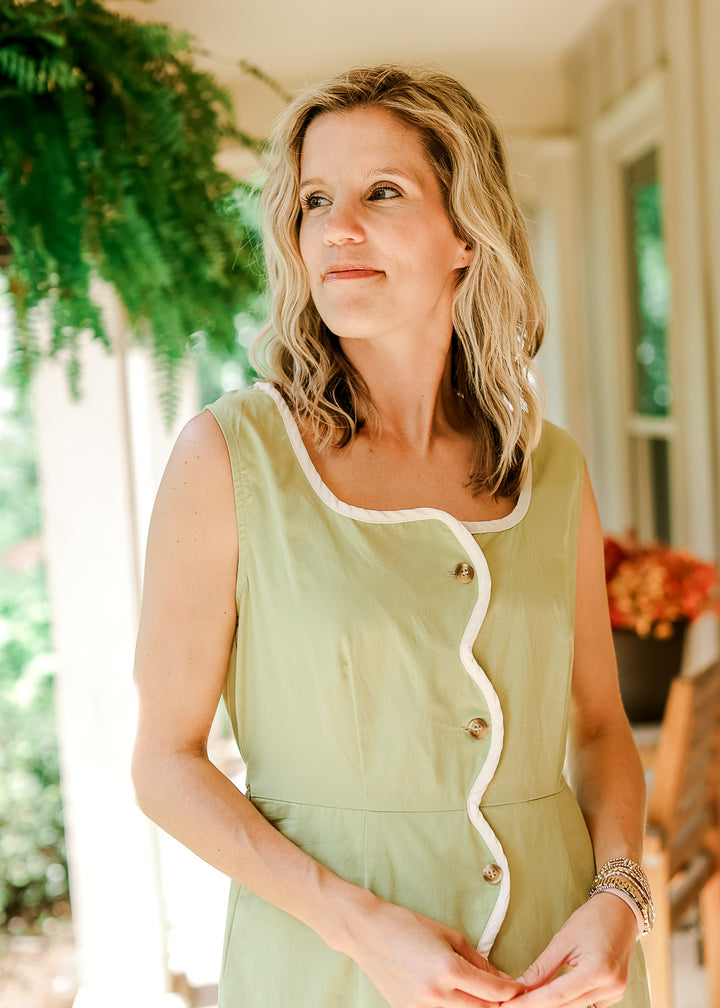 Model wearing a sleeveless light green midi with cream wavy piping, scoop neck and button front.