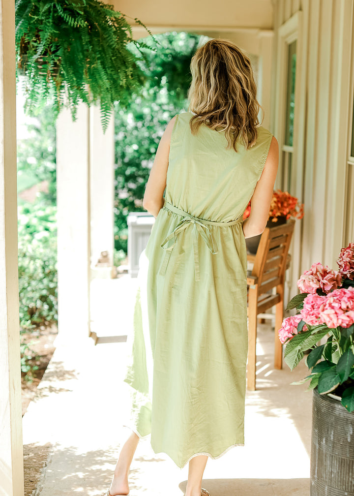 Back view of Model wearing a light green midi with a tie back and a sleeveless fit. 