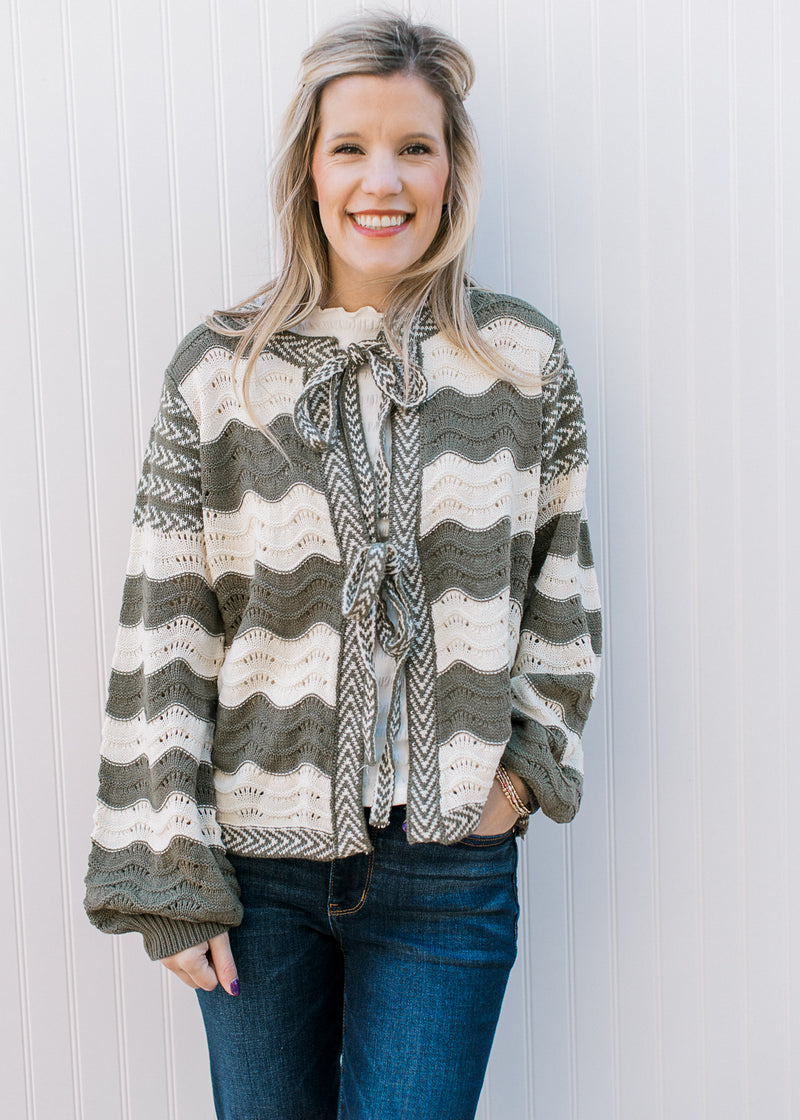 Model wearing an olive and cream wavy stripe cardigan with tie front and balloon long sleeves.