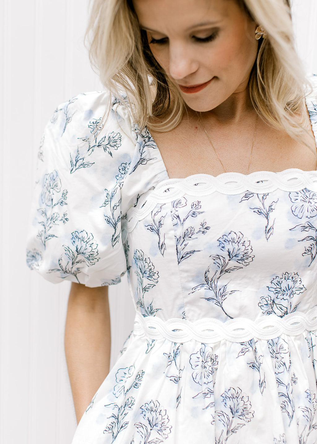 Close up of lace detailing at neck and waist of a cream top with blue floral and short puff sleeves.