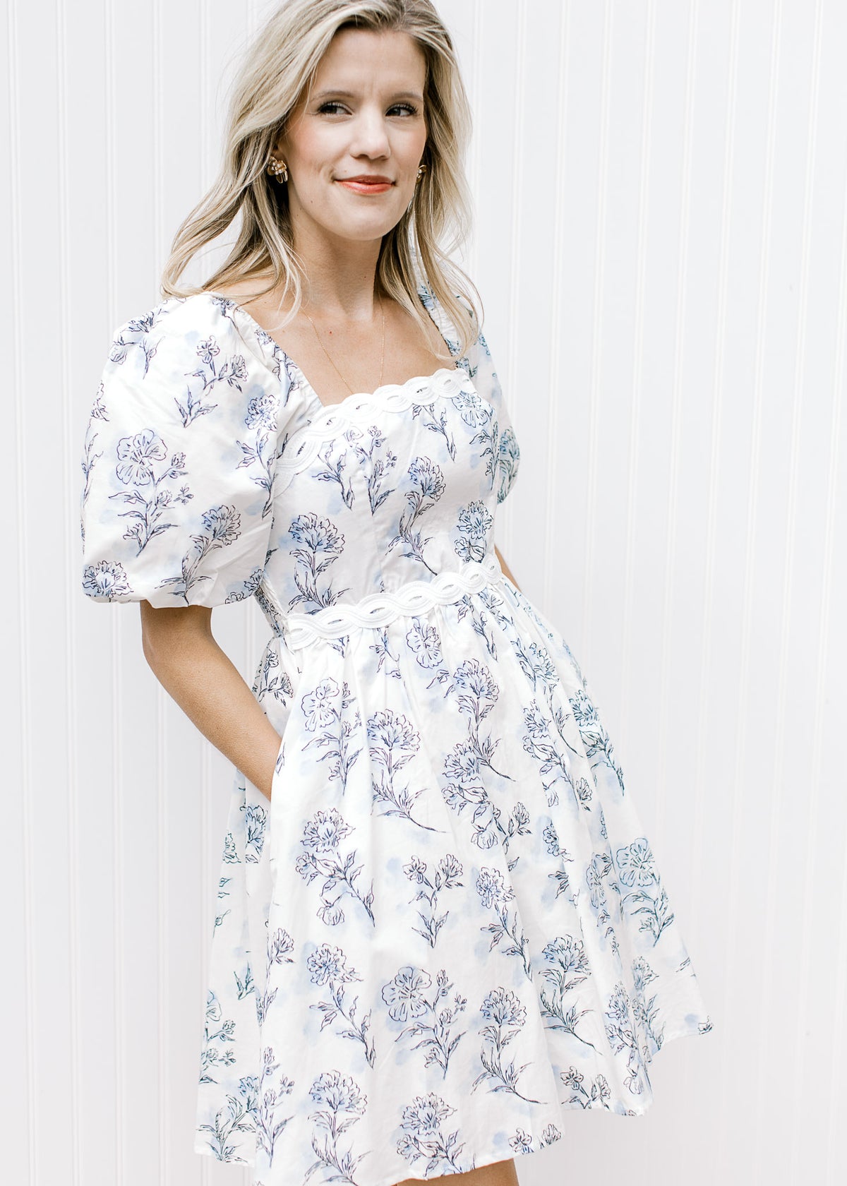 Model wearing a cream above the knee dress with pale blue floral, pockets and short puff sleeves. 
