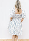 Back view of Model wearing a cream dress with pale blue floral square neck and smocked back.