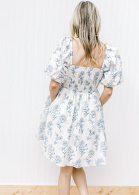 Back view of Model wearing a cream dress with pale blue floral square neck and smocked back.