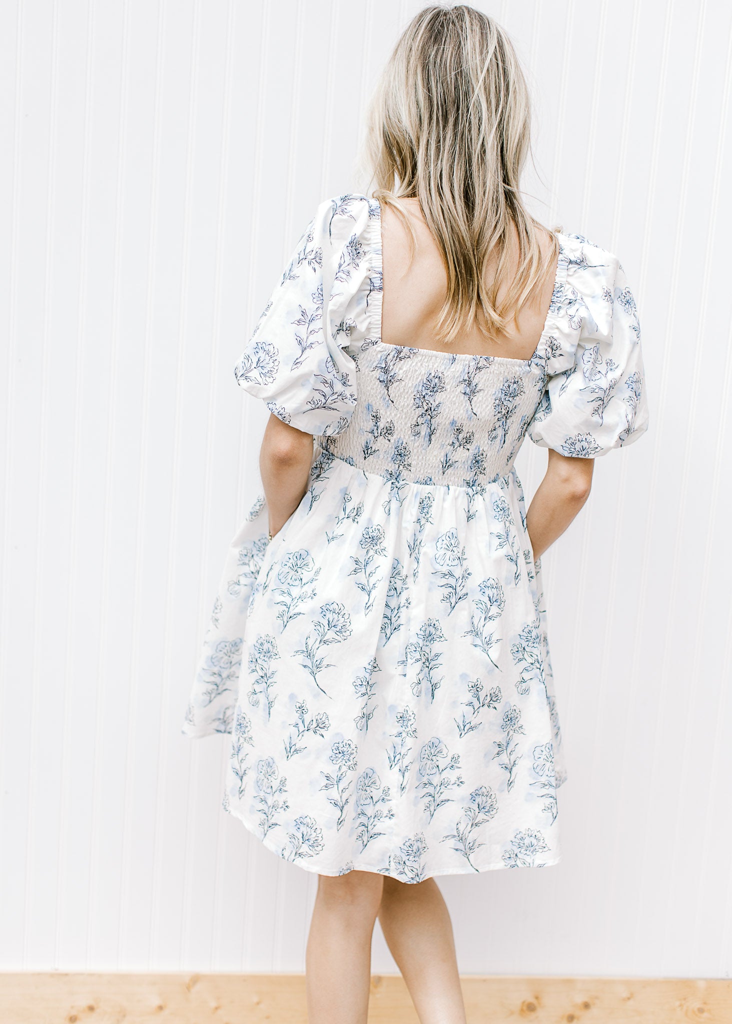 Back view of Model wearing a cream dress with pale blue floral square neck and smocked back.