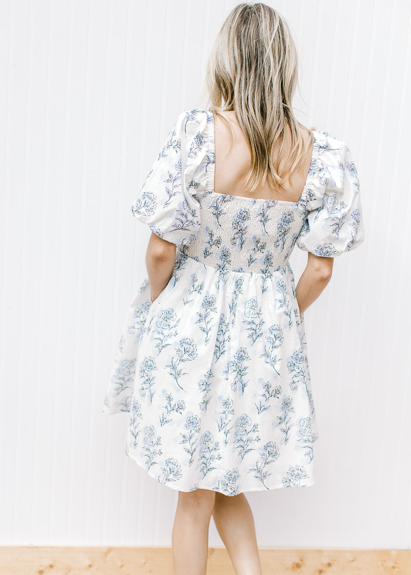 Back view of Model wearing a cream dress with pale blue floral square neck and smocked back.