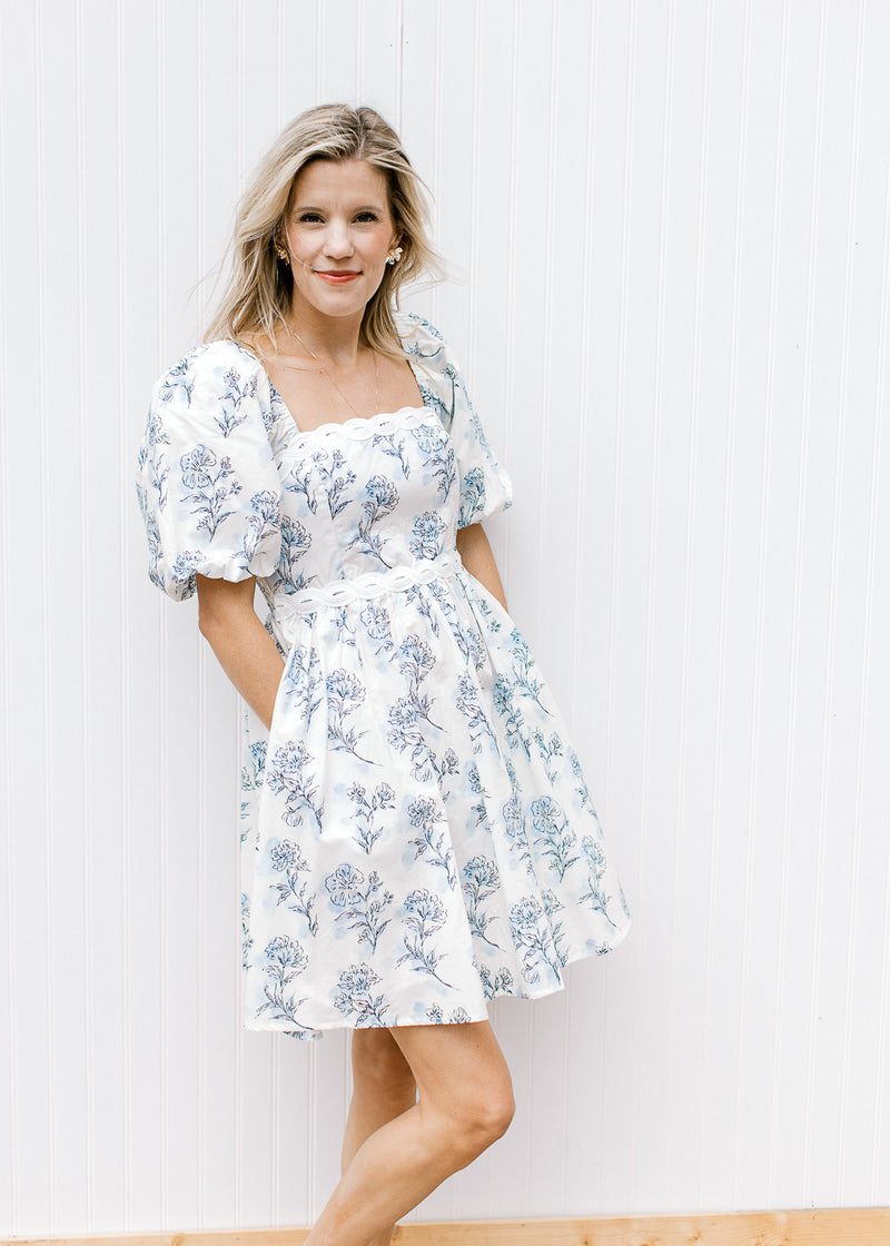 Model wearing a cream above the knee dress with pale blue floral square neck and short sleeves. 
