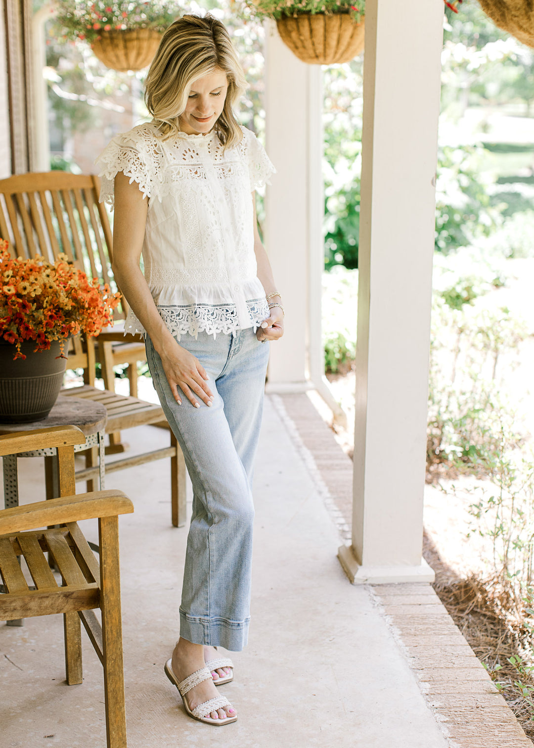 Model wearing jeans, sandals and a white top with eyelet detailing and floral lace accents.