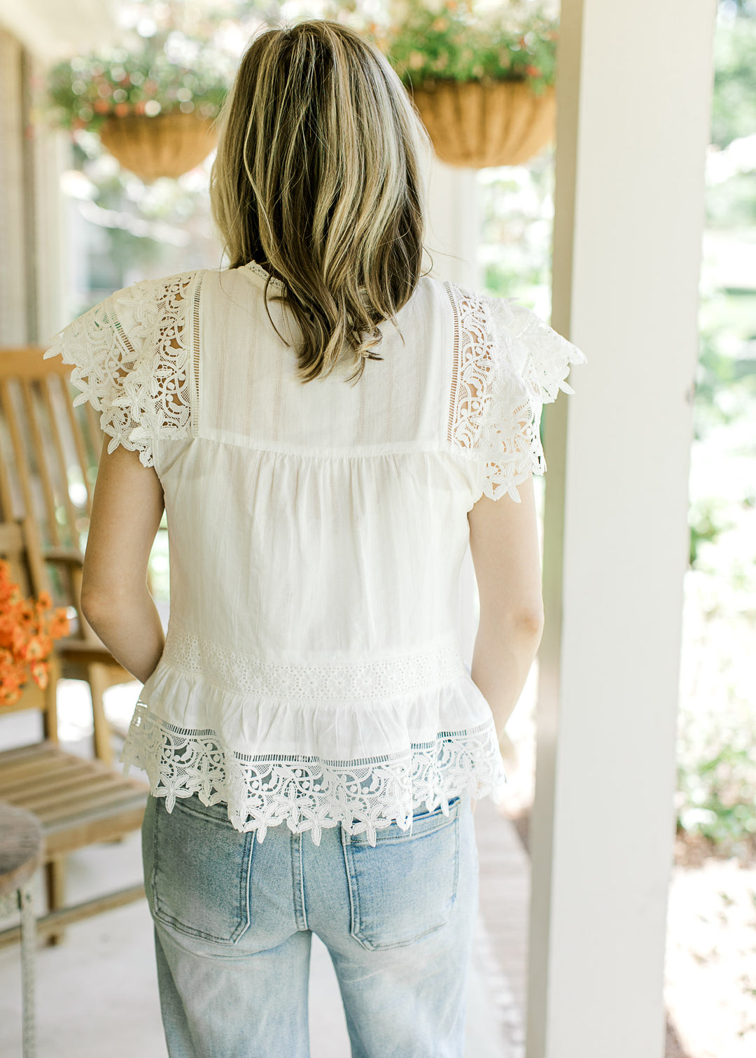 Back view of Model wearing a white top with eyelets, floral lace accents and lace cap sleeves.