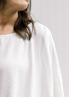 Model wearing a white polyester top with batwing short sleeves and a round neck. 