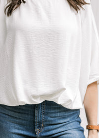 Close up of detail at the waist on a white polyester top with short batwing sleeves. 