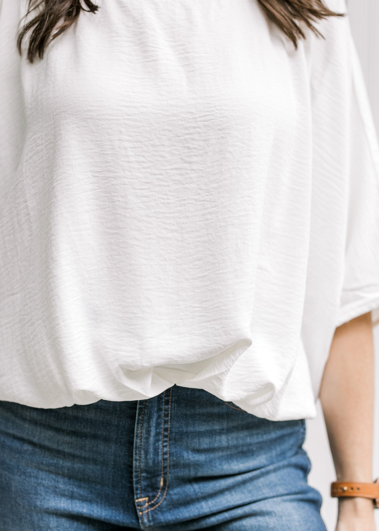 Close up of detail at the waist on a white polyester top with short batwing sleeves. 