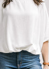 Close up of detail at the waist on a white polyester top with short batwing sleeves. 