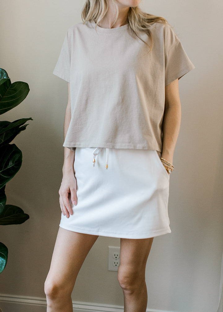 Model wearing a tan top with a white skort with elastic waist with tie, built-in shorts and pockets.