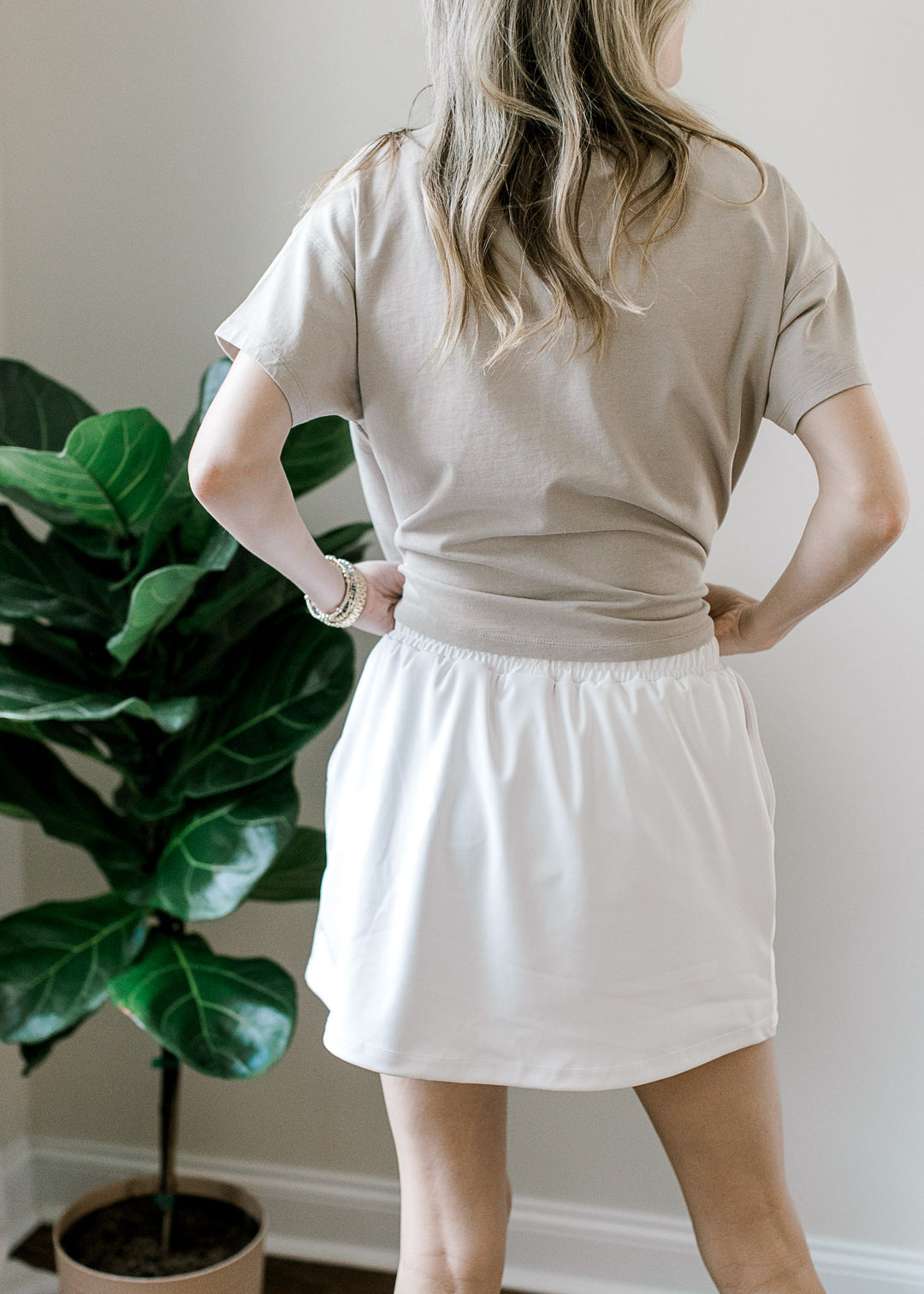 Back view of Model wearing a white skort with elastic waist with tie, built-in shorts and pockets.