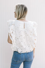 Back view of Model wearing a white top with a lace flower cut out and layered cap sleeves.