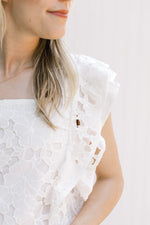 Close up of flower lace cut out on a white top with a square neck and layered cuff sleeves.