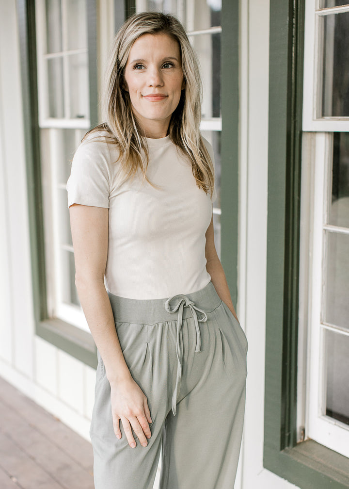 Model wearing an off white tee with a ribbed material, short sleeves and a round neckline.