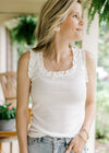 Model wearing a white sleeveless ribbed top with ruffle at sleeves and neck and a bow at neck. 