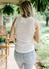 Back view of Model wearing a white ribbed top with ruffle at sleeves and neck and a bow at neck. 