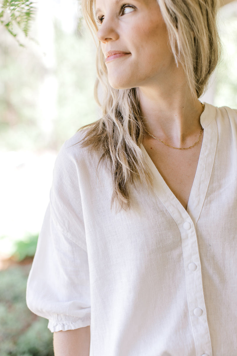 Close up of v-neck on a button up cool white top with short sleeves and an elastic cuff. 