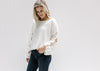 Model wearing a white sweater with long floral crochet sleeves, a crop fit and a wide round neck. 