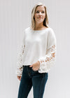 Model wearing jeans and a white crop sweater with long floral crochet sleeves and a wide round neck.