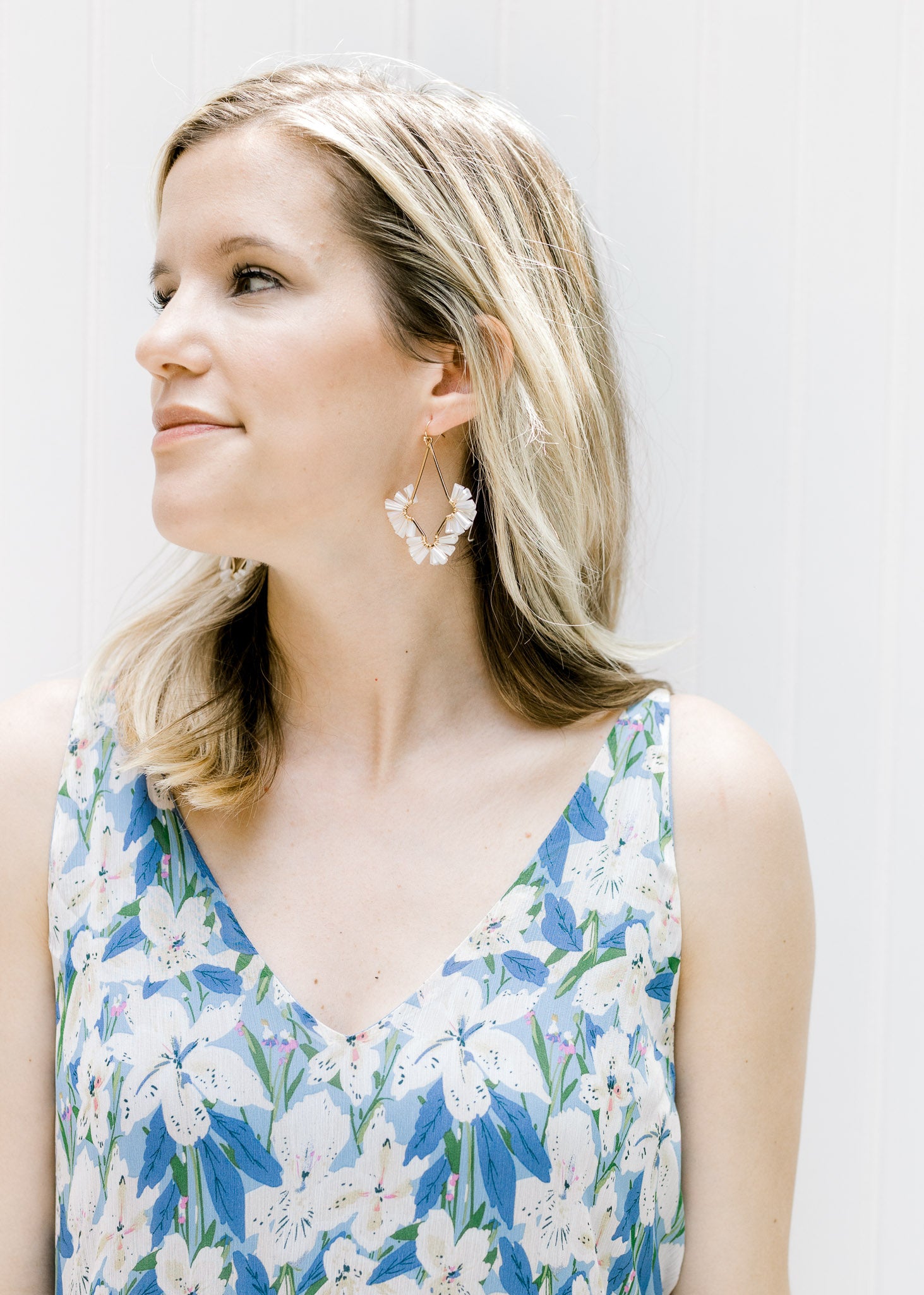 Model wearing gold wire dangle earrings with white fan beaded detail. 
