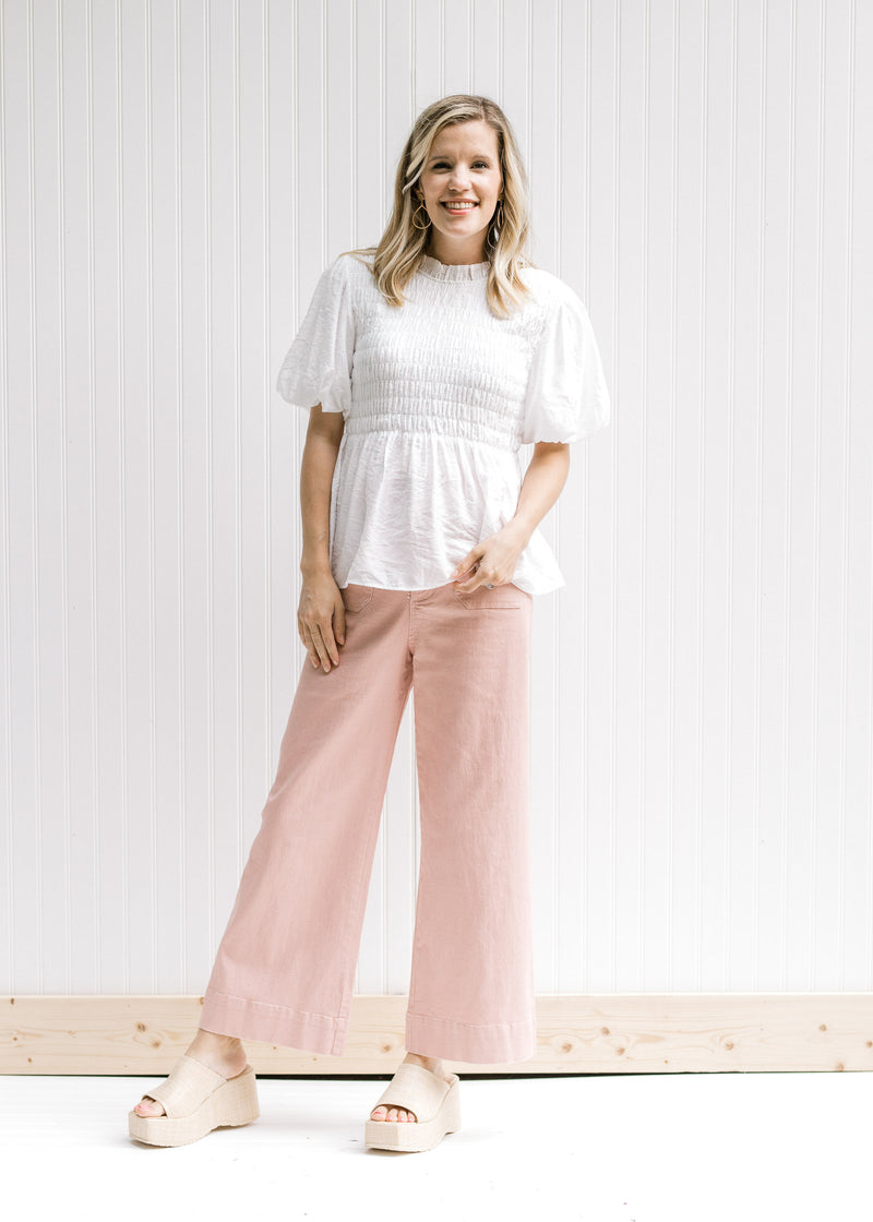 Model wearing pink bottoms and a white top with puff short sleeves and a round neck with a ruffle. 