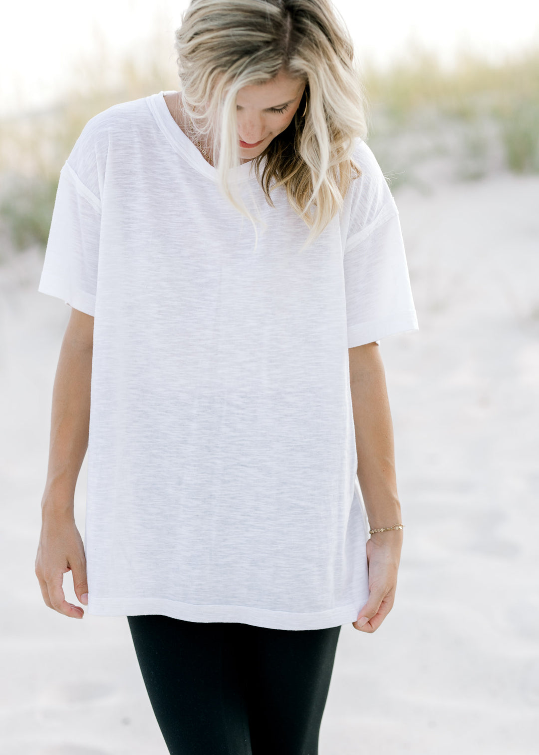 Model wearing a white, hi-low workout top with exposed seam, short sleeves and split sides. 