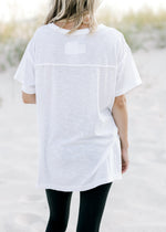 Back view of Model wearing a white workout top with exposed seam, short sleeves and split sides. 