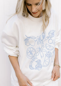 Model wearing a white sweatshirt with fruit embroidered in blue and matching short set.
