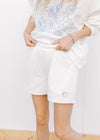 Model wearing an ultra soft white sweatshirt/short set with fruit embroidered in blue. 