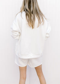 Back view of model wearing a white sweatshirt/short set with fruit embroidered in blue. 