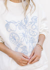Close up of blue embroidered fruit on a white sweatshirt with matching shorts with elastic waist. 
