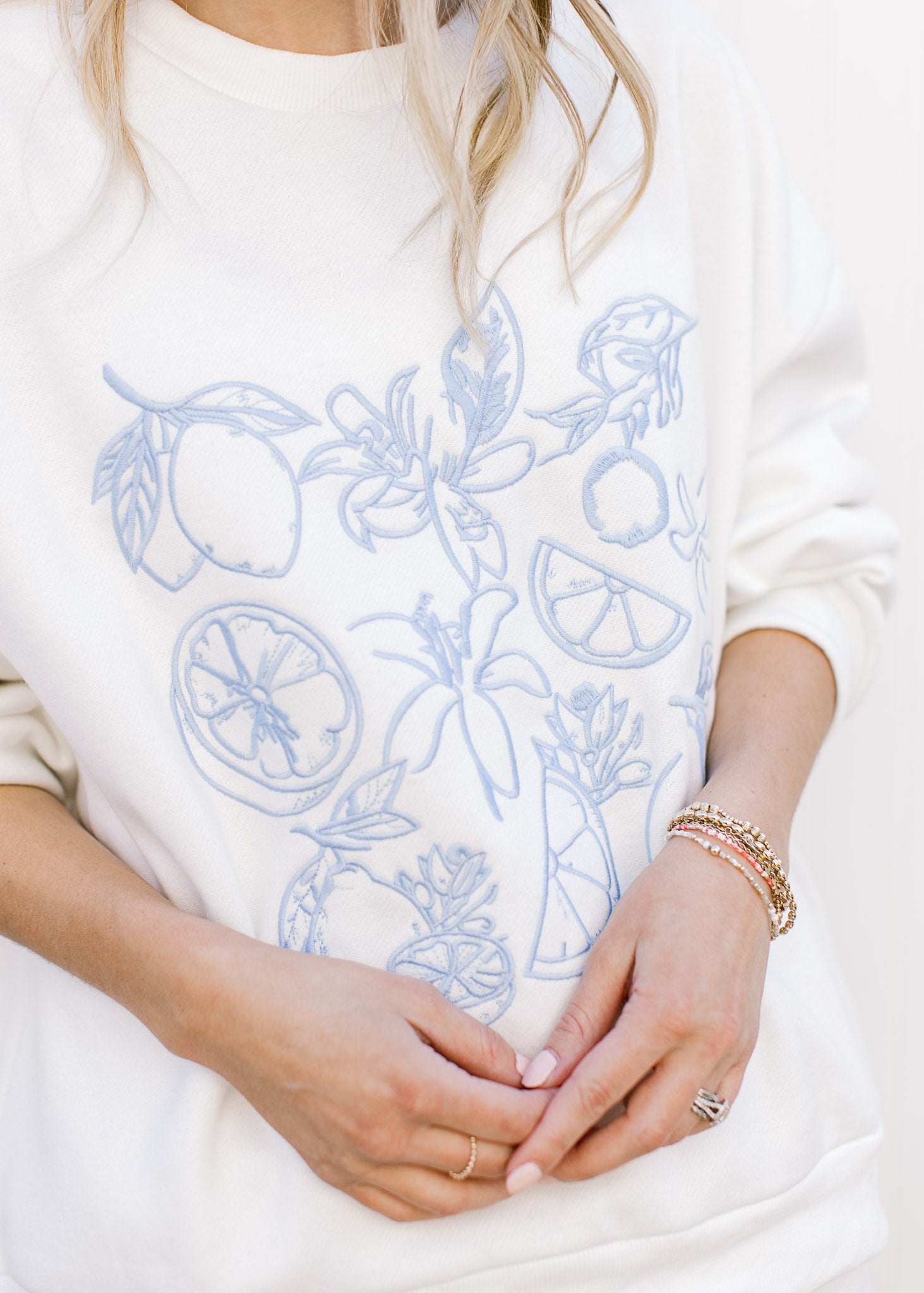 Close up of blue embroidered fruit on a white sweatshirt with matching shorts with elastic waist. 