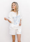 Model wearing a lightweight white sweatshirt/short set with fruit embroidered in blue. 