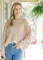 Model wearing a taupe knit sweater with embroidered daises round neck and long sleeves. 