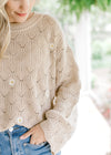 Close up of embroidered daises on a taupe top with round ribbed neck and long sleeves.