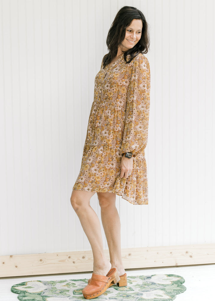Model wearing a chestnut v-neck dress with a natural floral pattern with sheer long sleeves.
