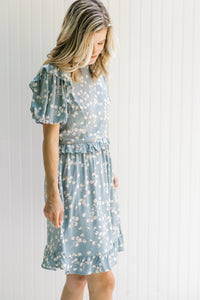 Model wearing a light blue, above the knee dress with cream floral and bubble short sleeves.
