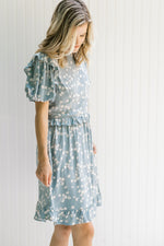 Model wearing a light blue, above the knee dress with cream floral and bubble short sleeves.
