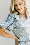 Close up view of ruffle detail at shoulder and waist of a light blue dress with cream floral. 